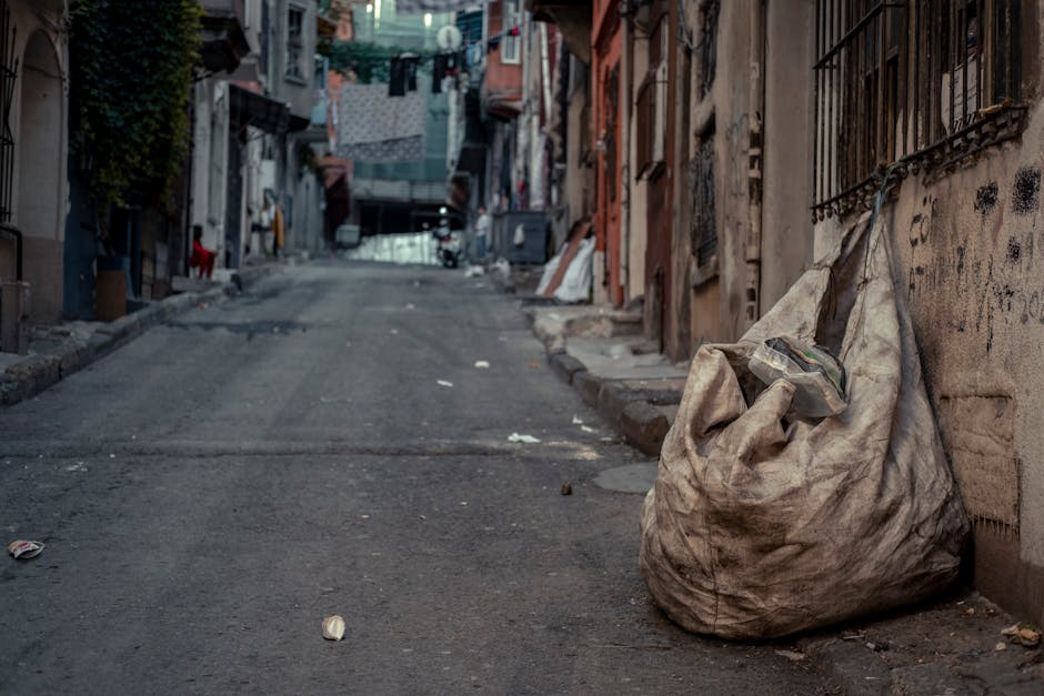 A close-up image of several black plastic rubbish bags tightly tied at the tops, placed against a plain, light-colored wall. The bags are made of shiny, smooth plastic material, reflecting light on th